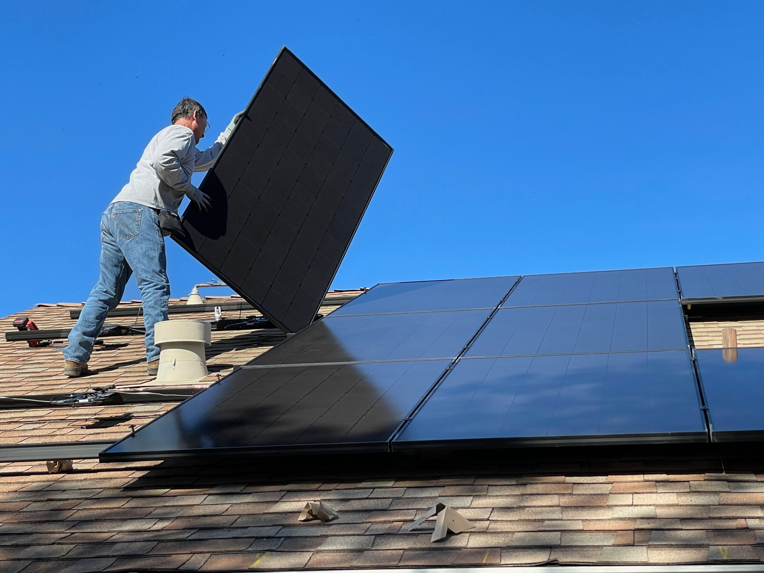 Workman setting a solar panel in place on the roof of a home.